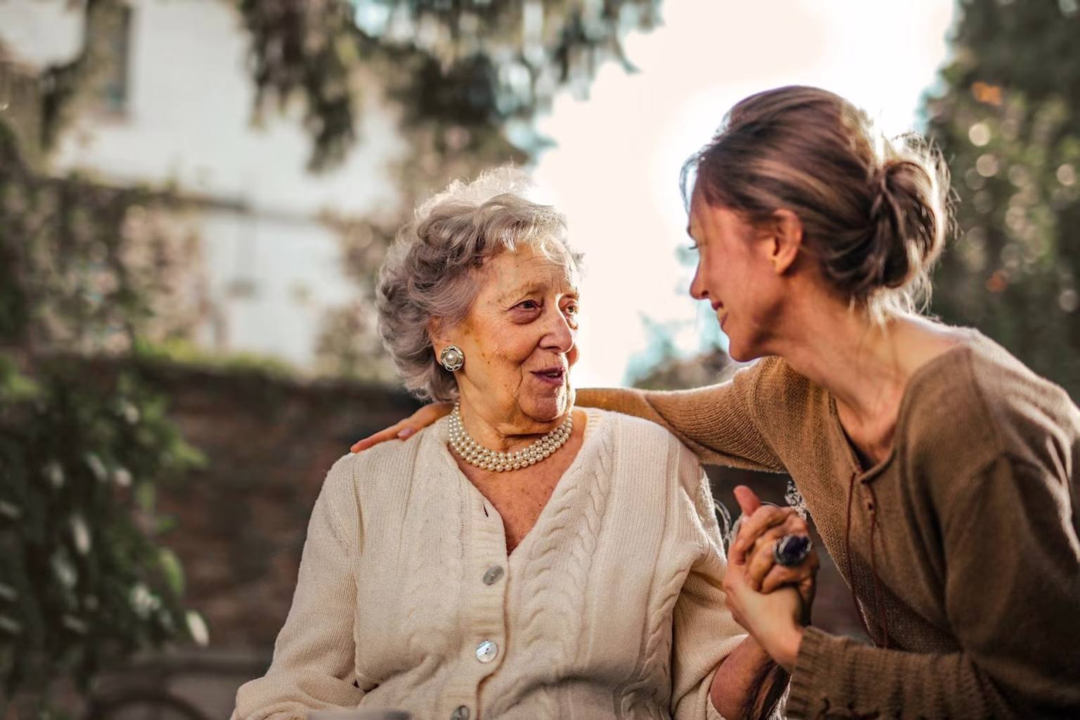 Daughter holding elderly mother's hand while sitting outside.