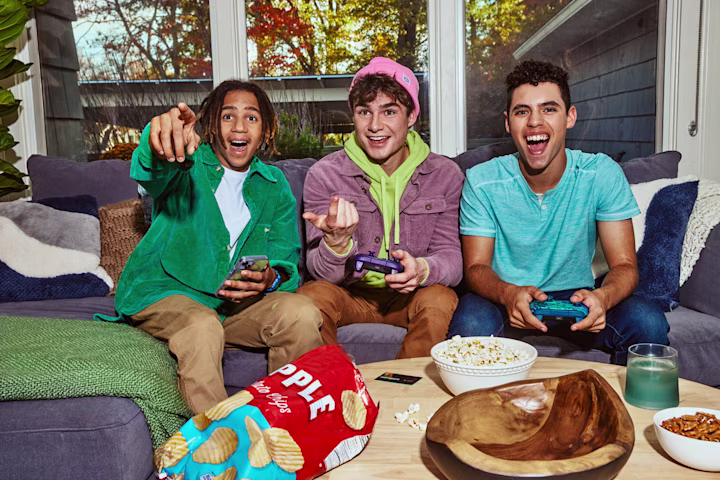 3 boys sitting on a couch playing video games.