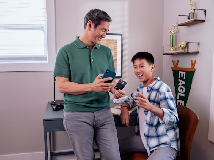 Father and son talking in bedroom while holding GL card.