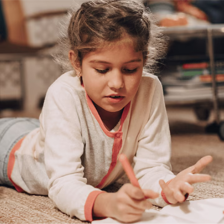girl writing in a notebook while lying on the floor