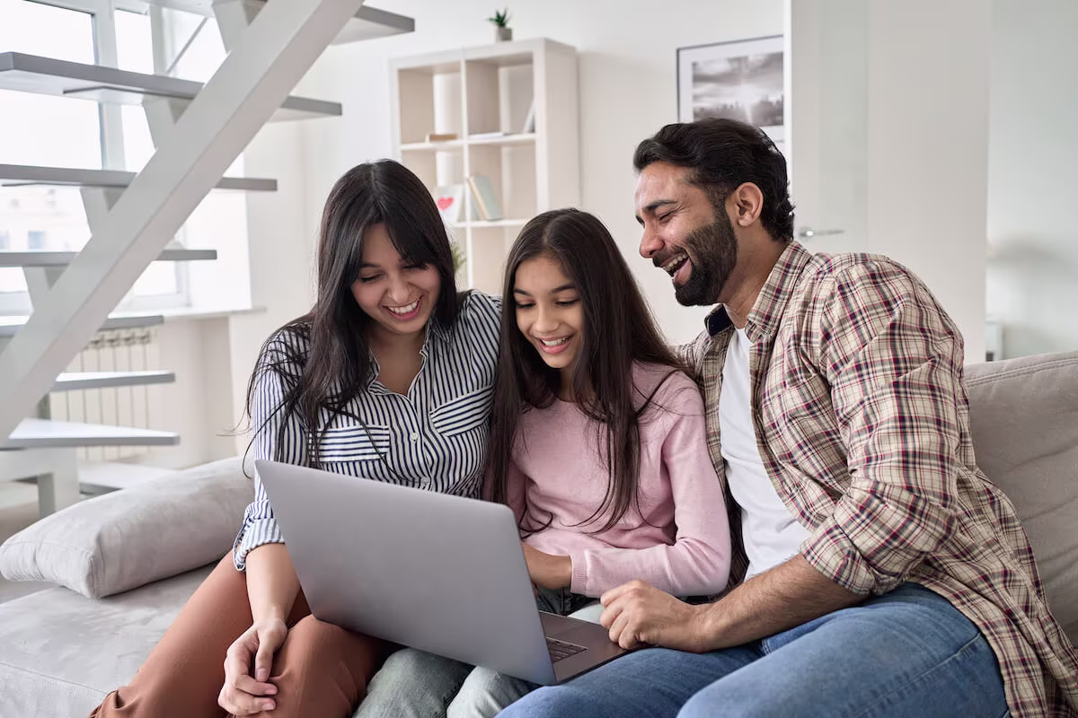 Parents happily supervising their daughter while she uses a laptop