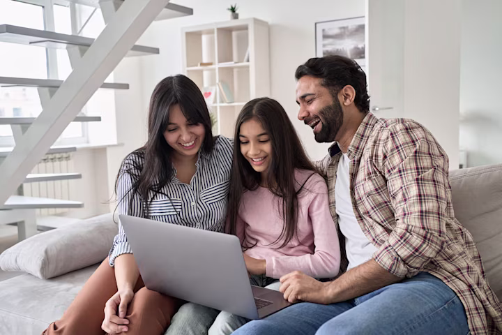 Parents happily supervising their daughter while she uses a laptop