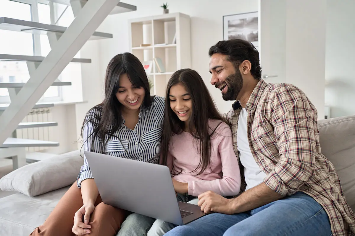 Parents happily supervising their daughter while she uses a laptop