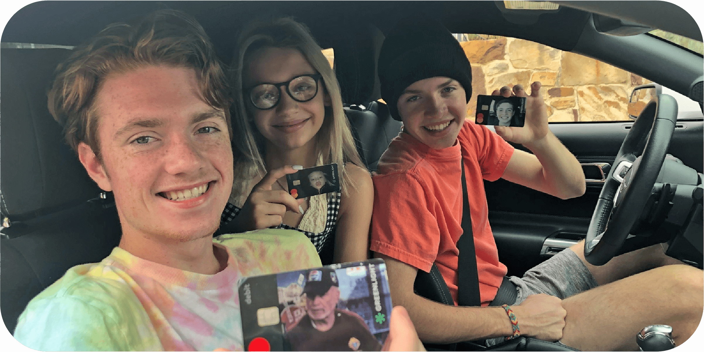 three teenagers in a car showing their Greenlight debit card for teens