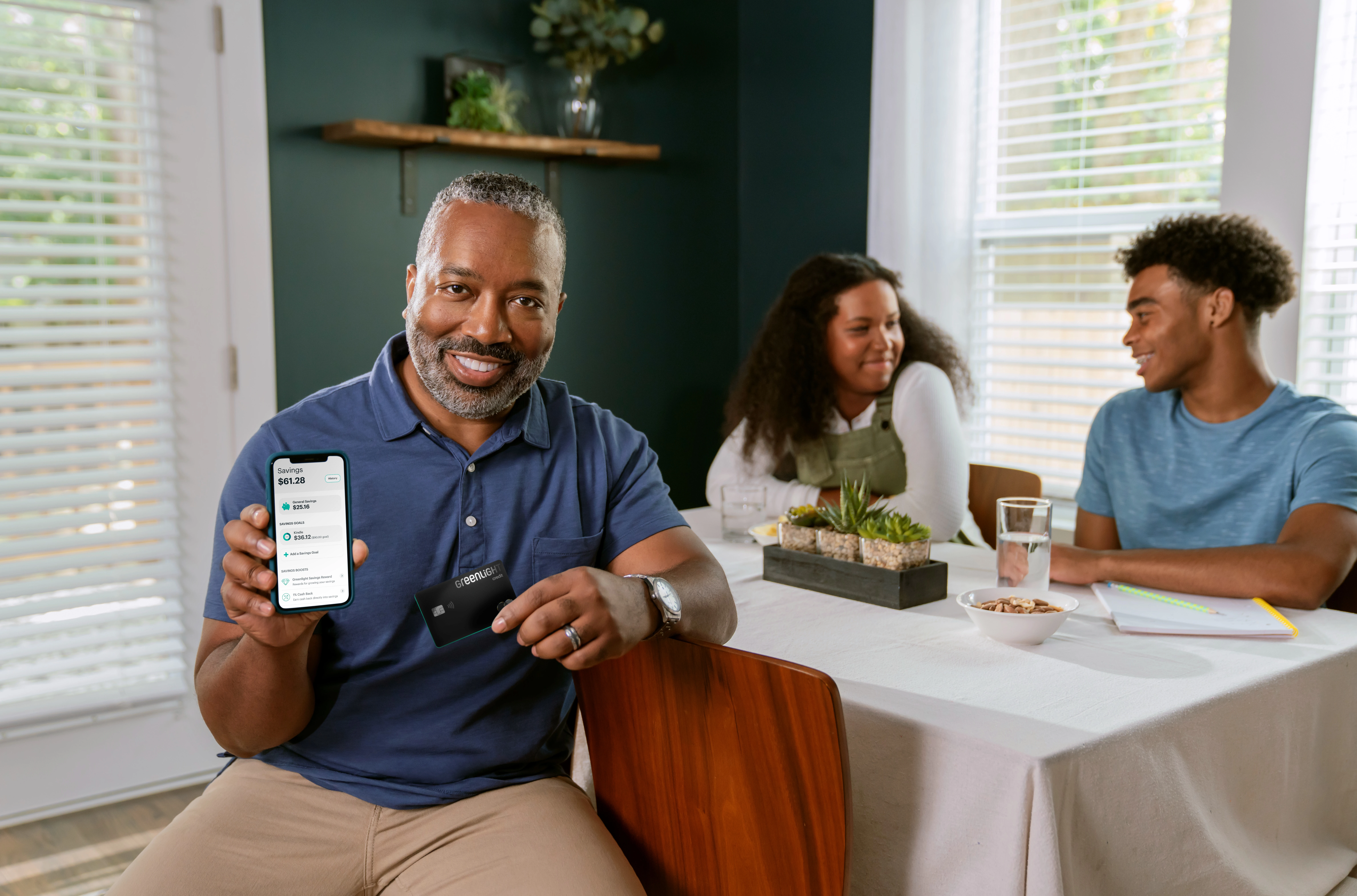 Dad shows off his parent dashboard on Greenlight app in living room with teen son and daughter