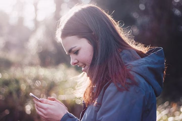 Teen girl standing outside looking at her phone.