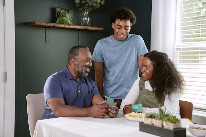 A family gathered around the table chatting and looking at a phone.
