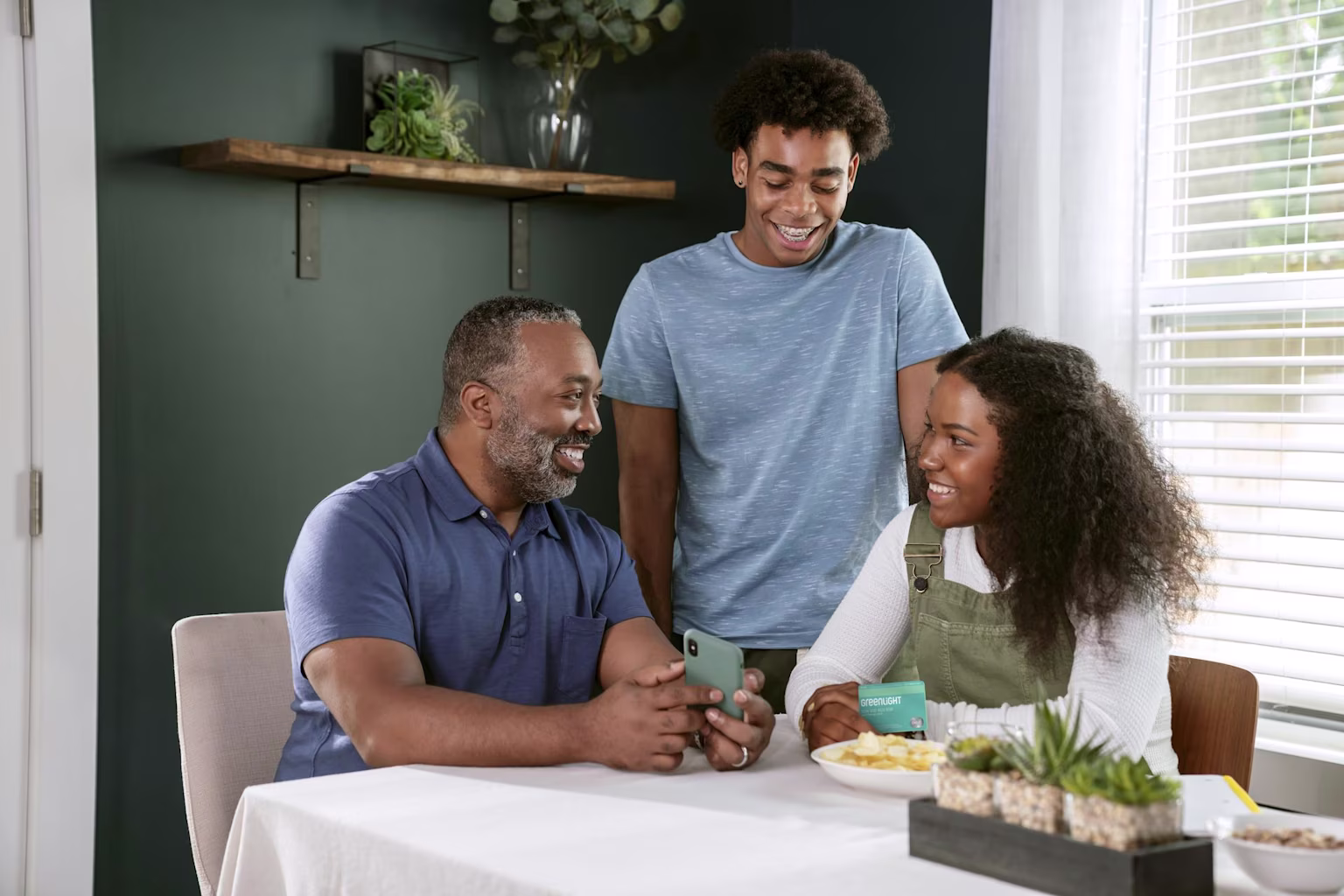 A family gathered around the table chatting and looking at a phone.