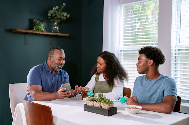 Teens talking to dad at the dinner table while holding Greenlight cards