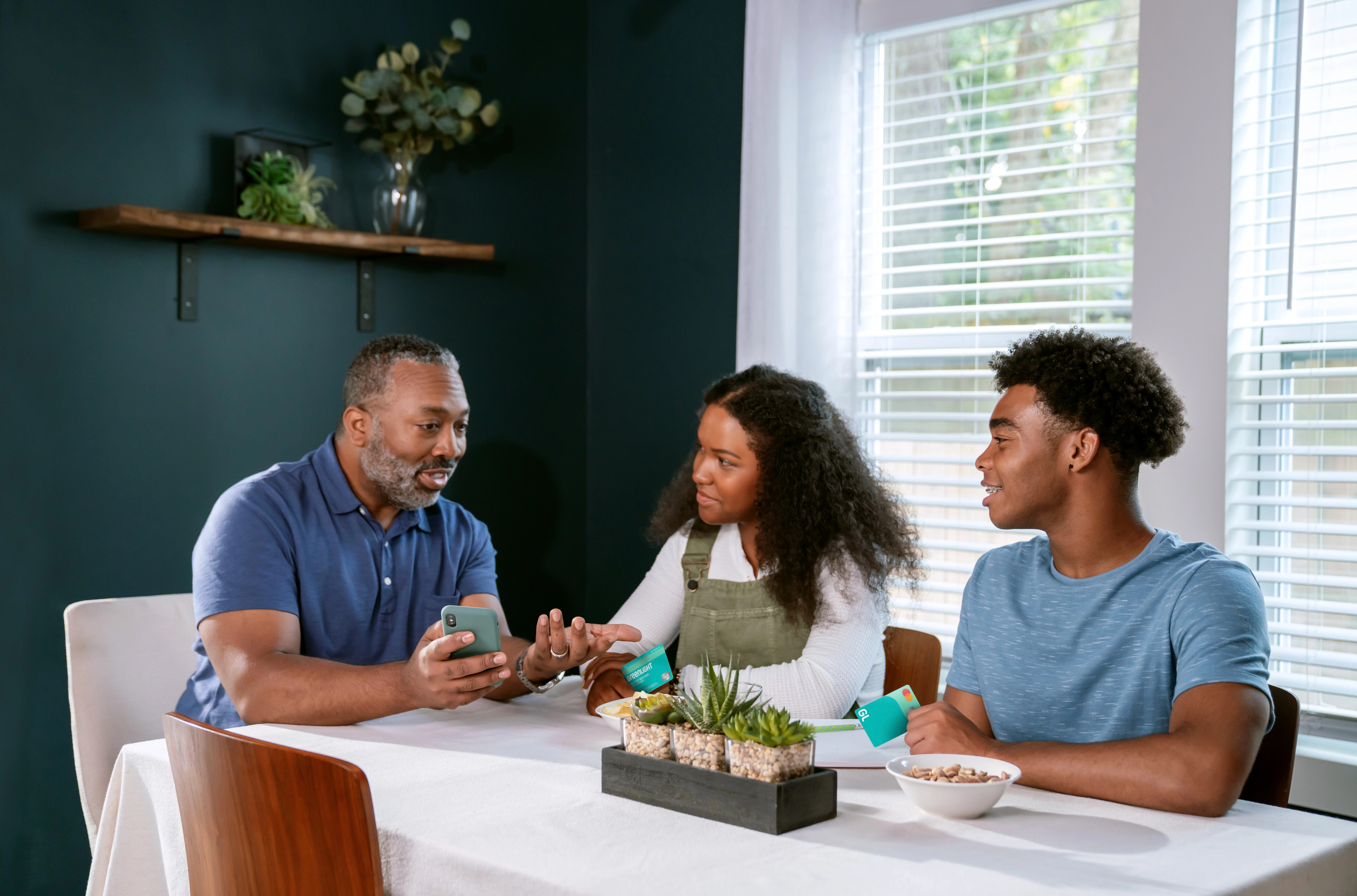 Teens talking to dad at the dinner table while holding Greenlight cards