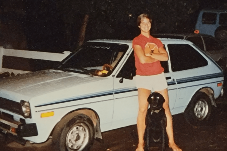 young man standing in front of his white car with his dog inbetween his legs