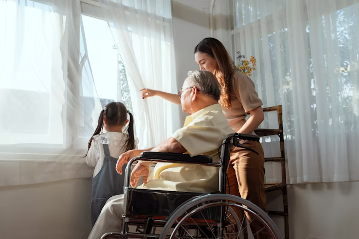 Woman, child & senior citizen in wheelchair looking out window.