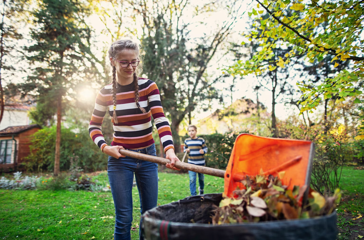 Girl raking leaves at home while making money with her brother