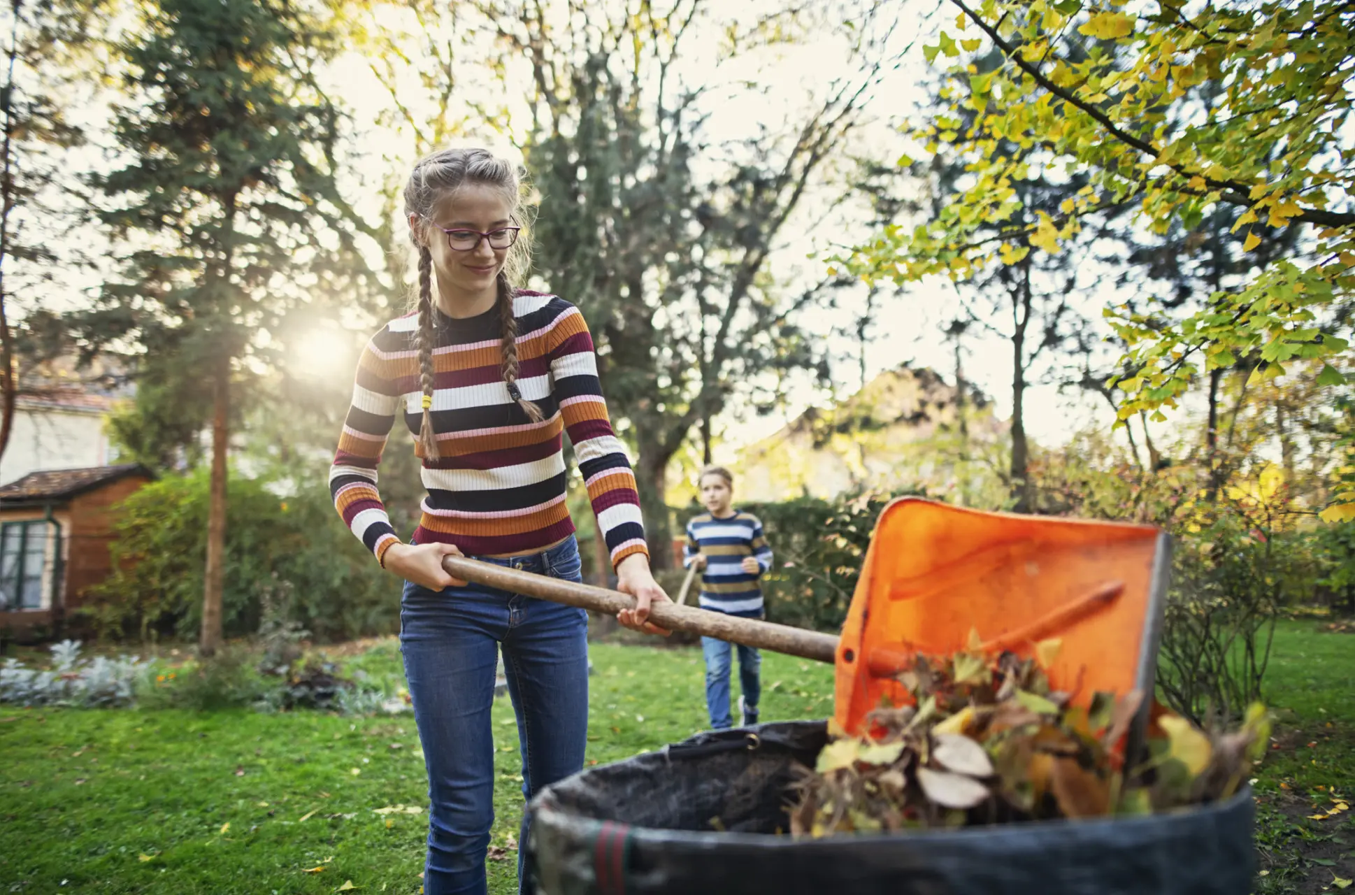 Girl raking leaves at home while making money with her brother