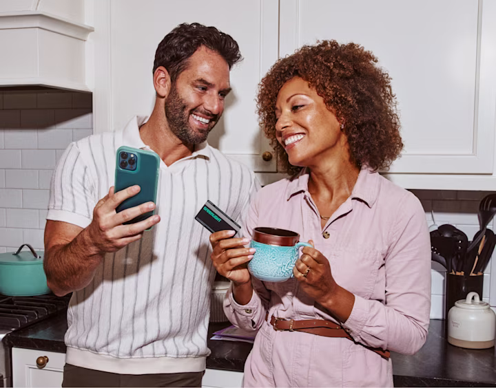 Parents in kitchen looking at phone with debit card and coffee
