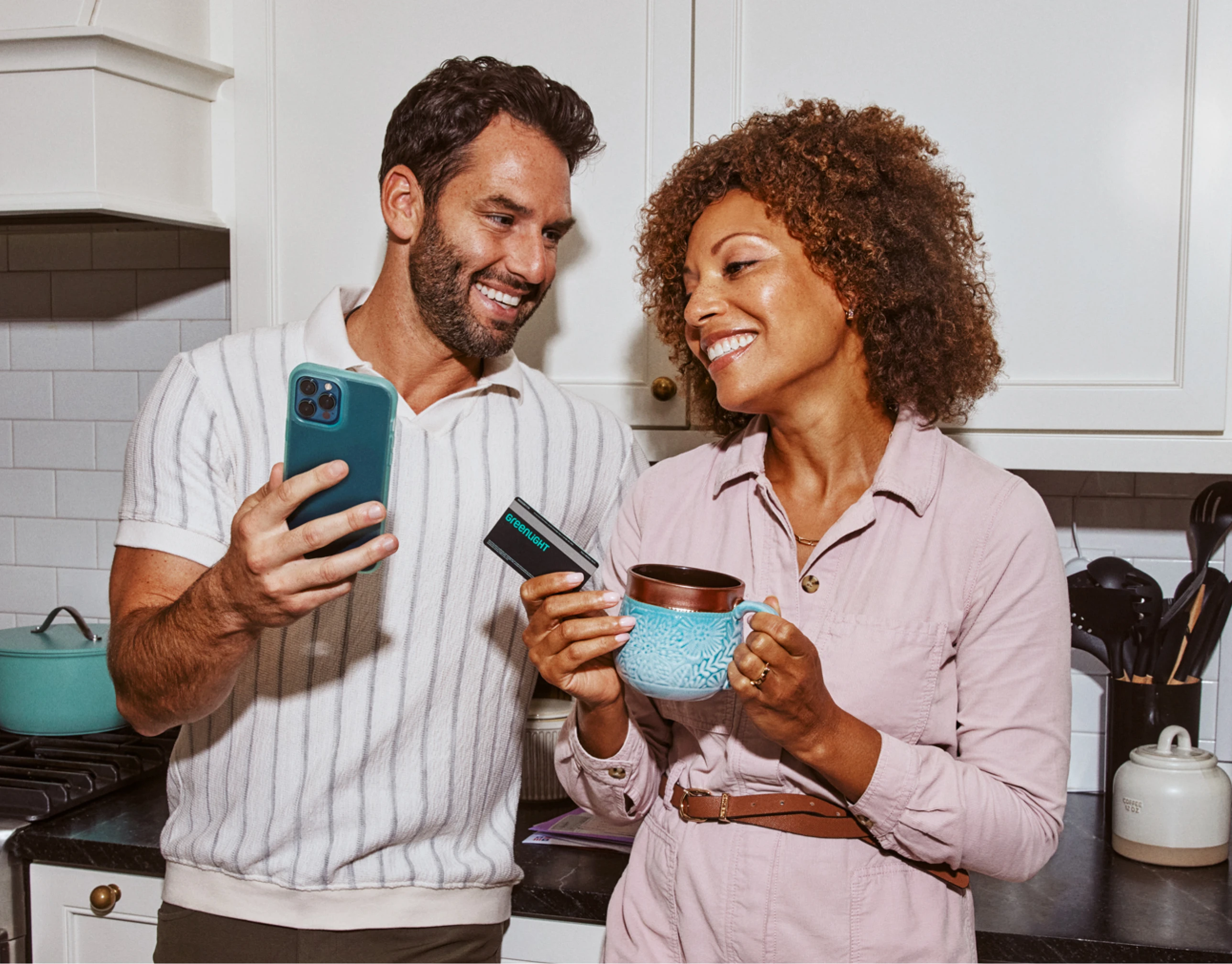Parents in kitchen looking at phone with debit card and coffee