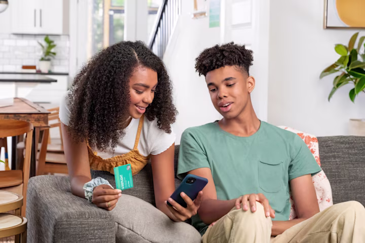 Teen boy and teen girl in living room looking at the Greenlight money app with financial literacy