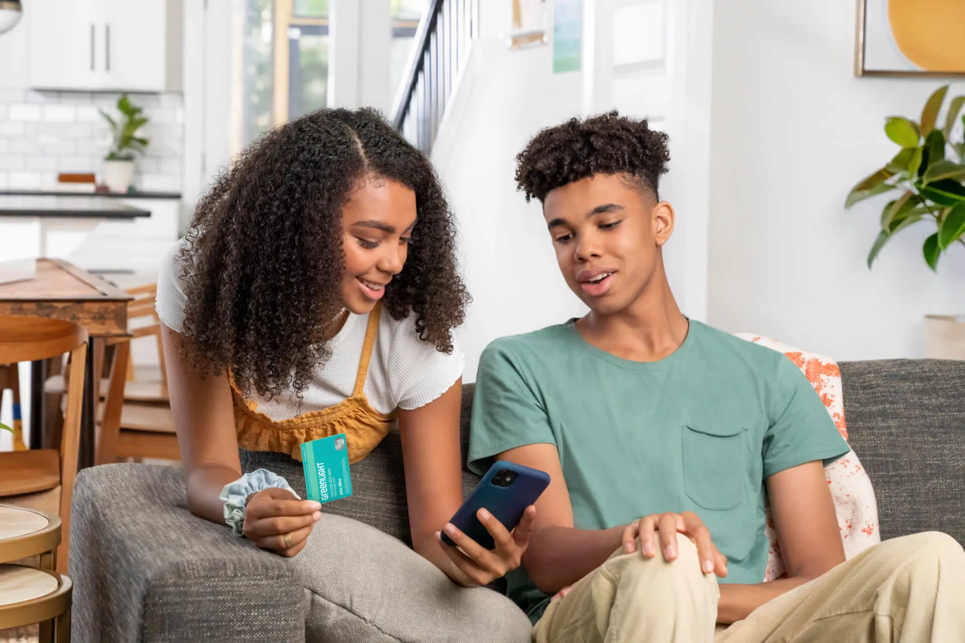 Teen boy and teen girl in living room looking at the Greenlight money app with financial literacy