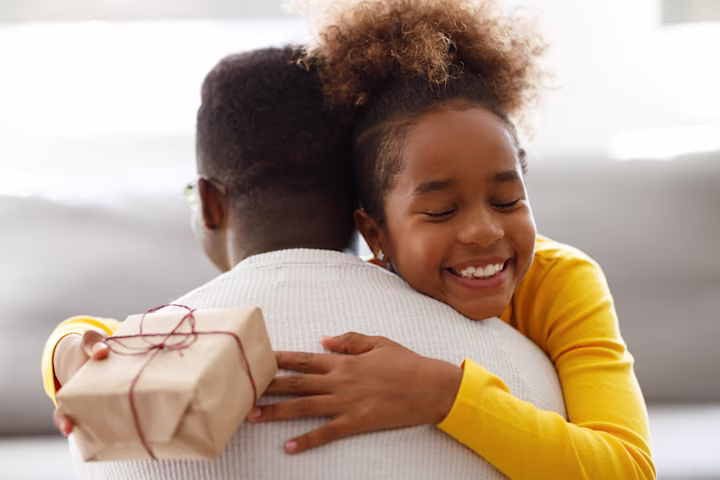 Girl holding gift while hugging a parent.