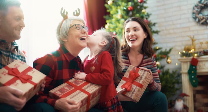 Christmas savings account: A young girl kisses her grandmother on the cheek while the family celebrates Christmas
