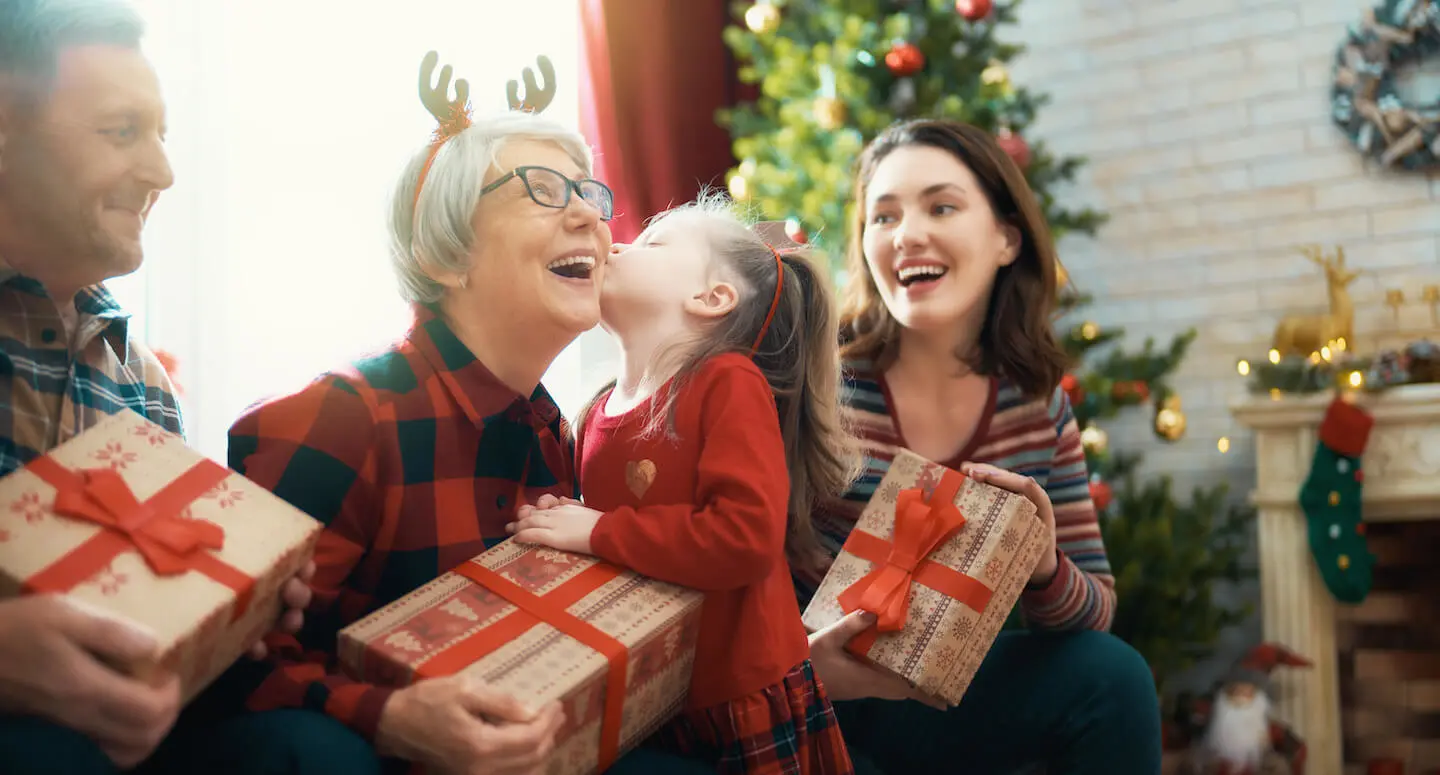 Christmas savings account: A young girl kisses her grandmother on the cheek while the family celebrates Christmas