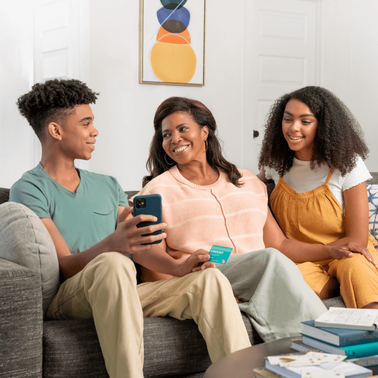 teenage son holding a smartphone and greenlight debit card with mother and teen girl