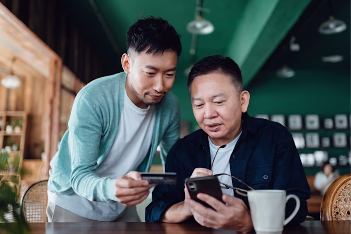 Elderly father and son looking at phone together in a restaurant.