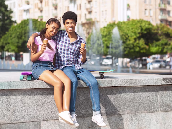 Two teens sit on the edge of a fountain and eat ice cream