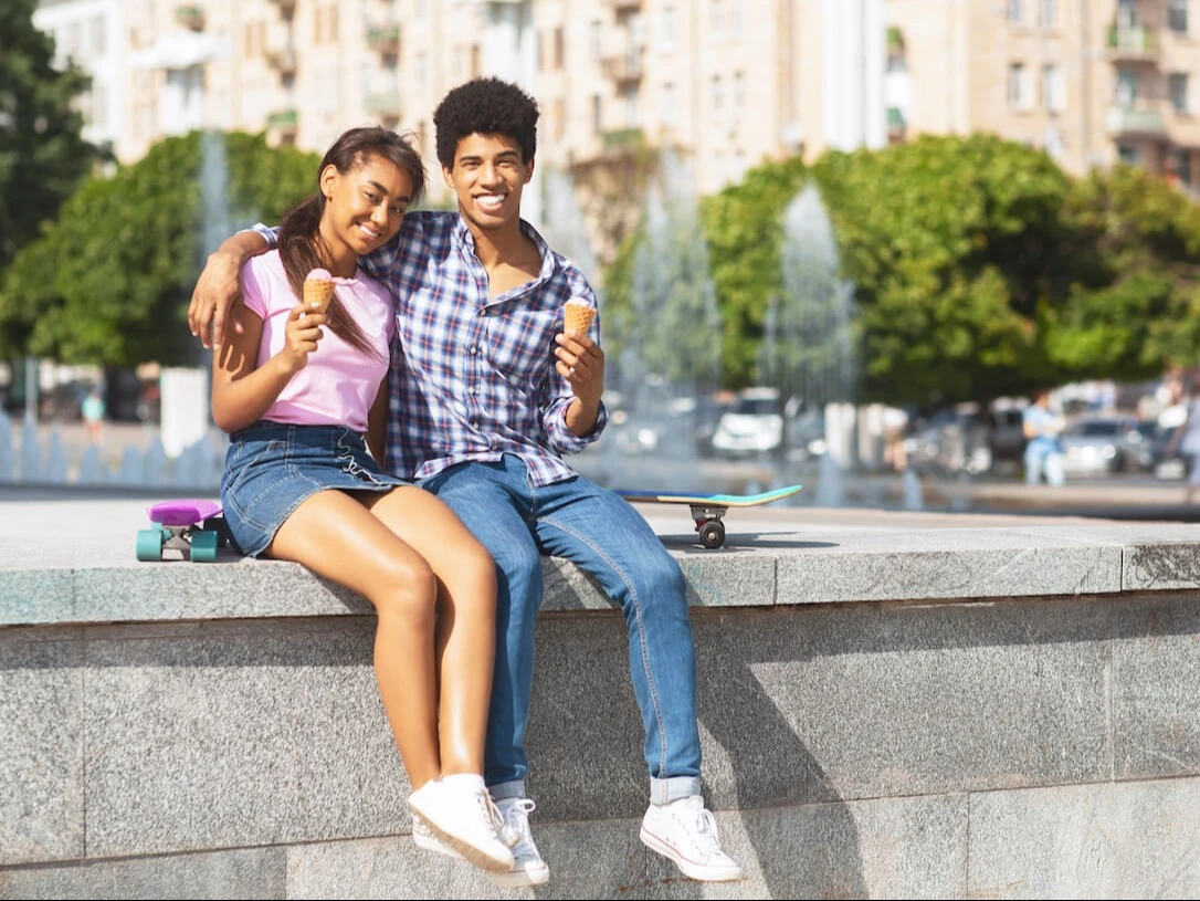 Two teens sit on the edge of a fountain and eat ice cream