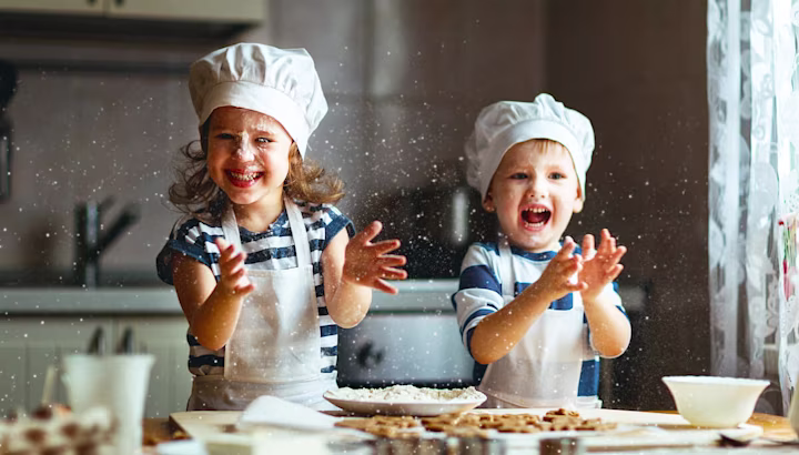A smiling sister and brother clap their hands while baking in the kitchen