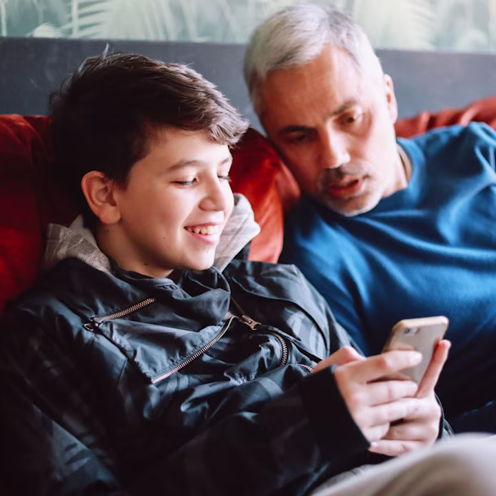 Dad and son on the couch looking at son's phone while talking about child identity protection and safety