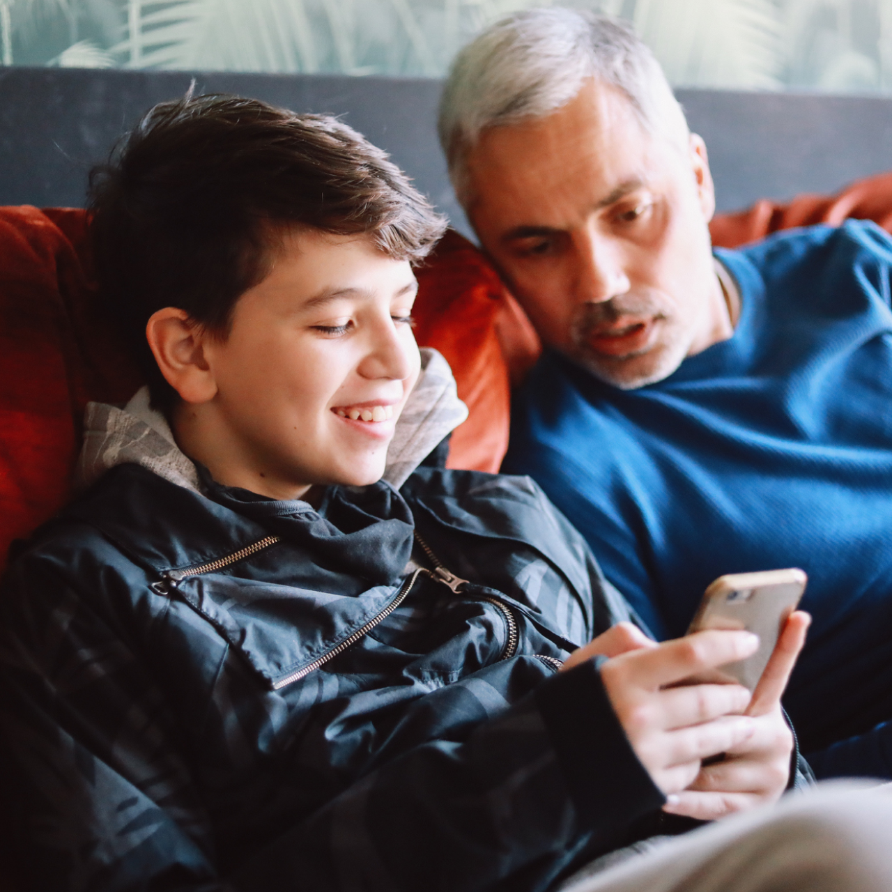 Dad and son on the couch looking at son's phone while talking about child identity protection and safety