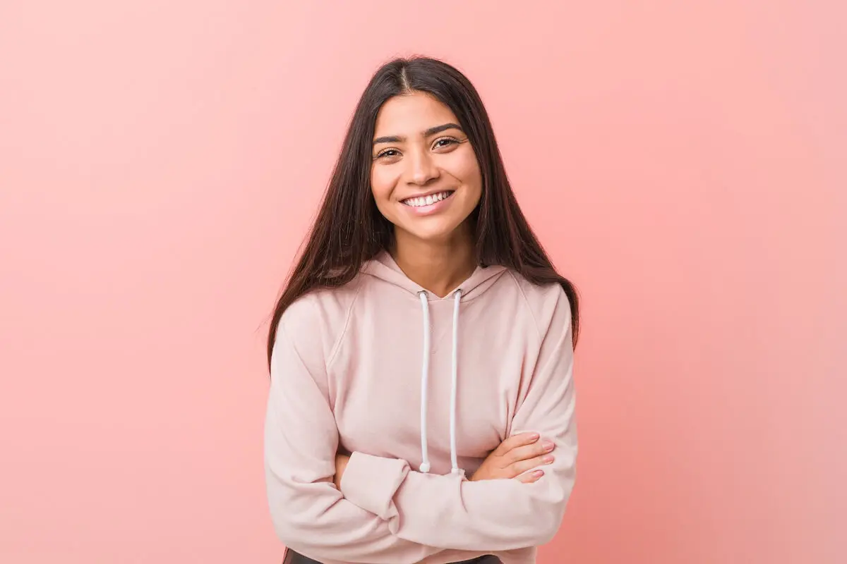 A teenage girl in a pink sweatshirt smiles at the camera