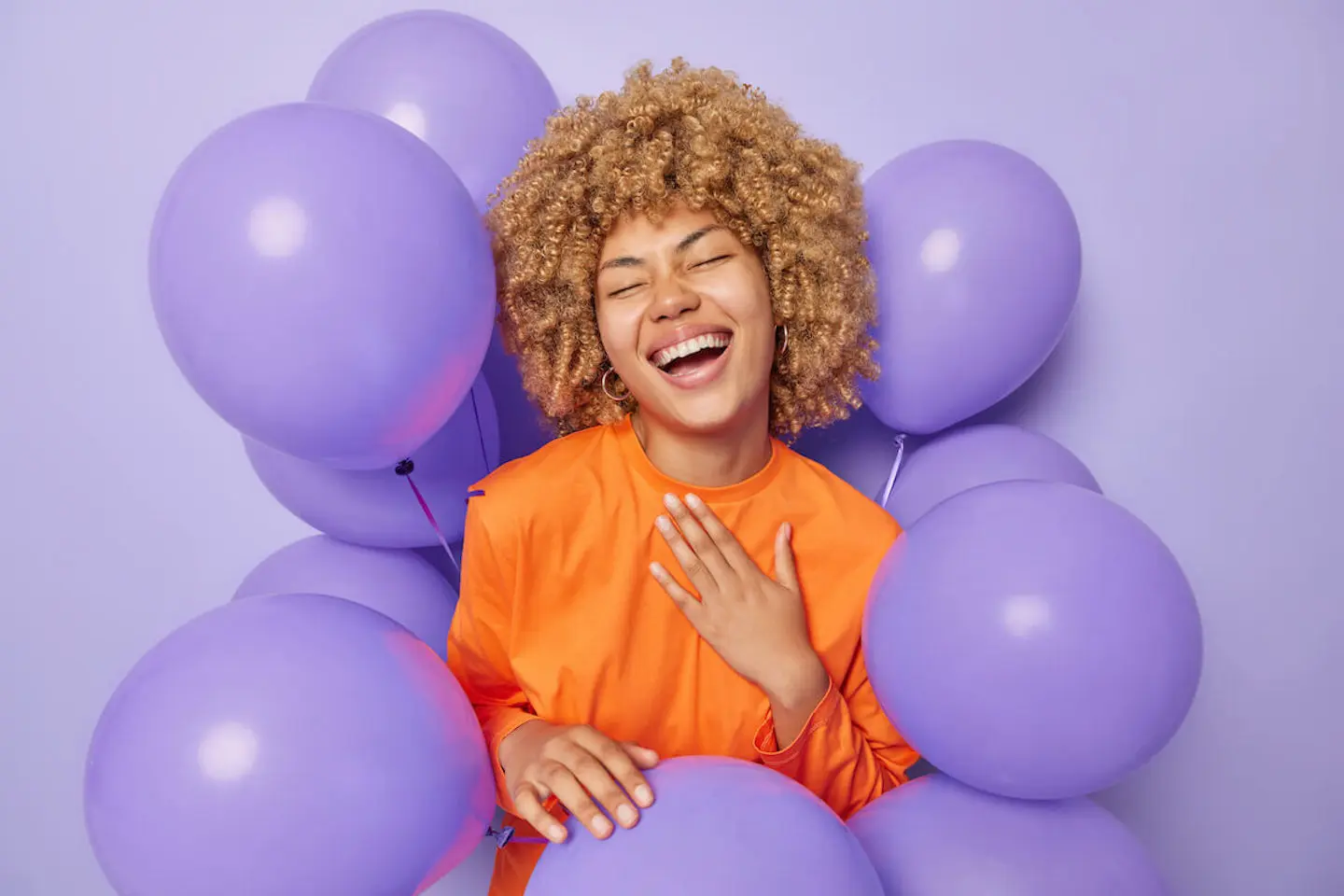 How to plan a birthday party: woman happily smiling with balloons surrounding her