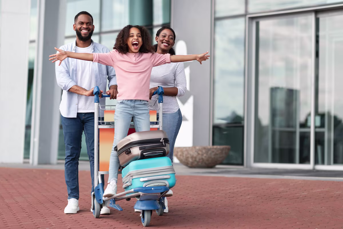 Parents pushing a baggage cart while their daughter is on it