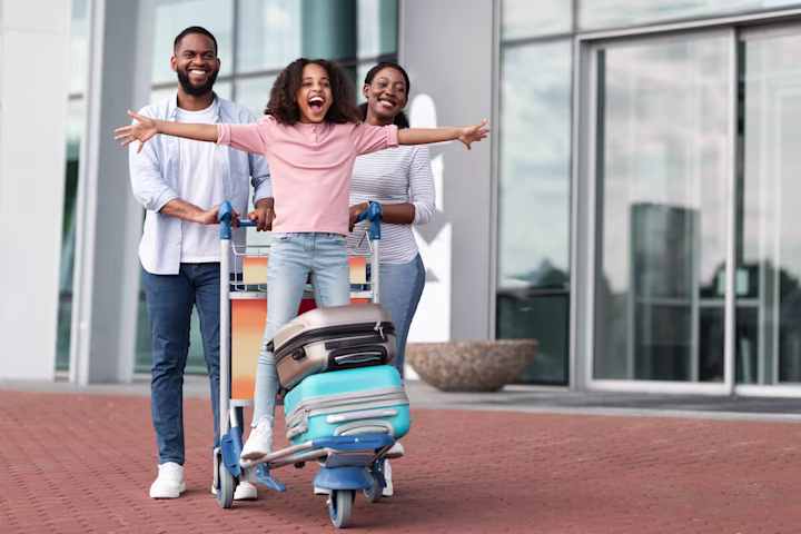 Parents pushing a baggage cart while their daughter is on it