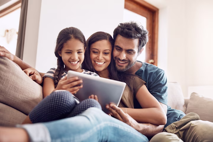 Mom, Dad and daughter smiling while looking at a tablet together.