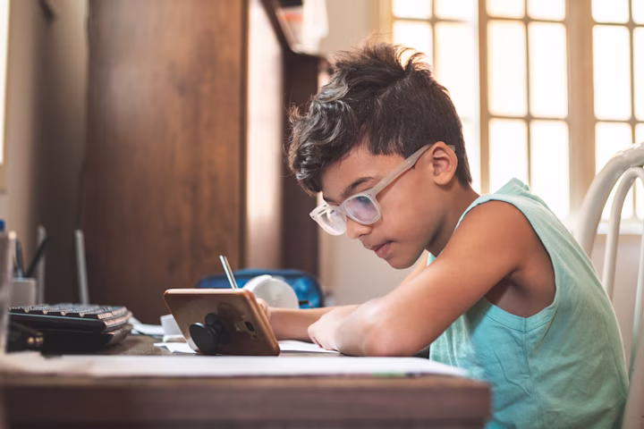 boy looking at his smart phone and writing in his notebook