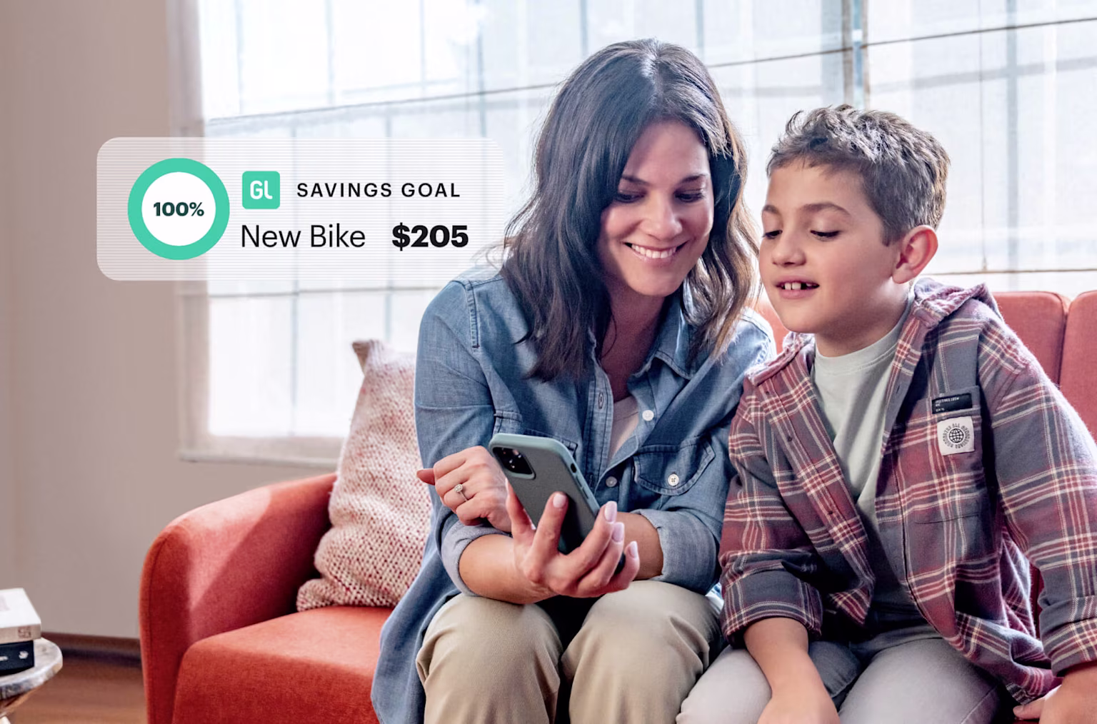 Mom and young son on the couch looking at the Greenlight financial literacy app and smiling at his Savings Goal