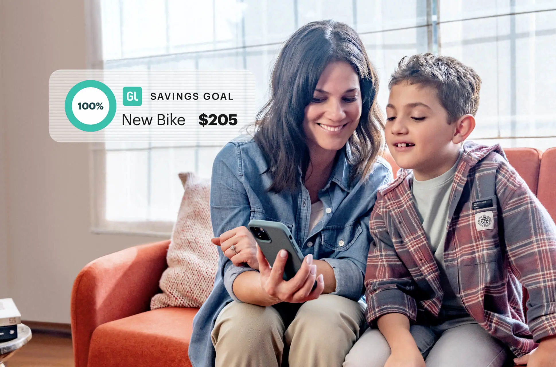 Mom and young son on the couch looking at the Greenlight financial literacy app and smiling at his Savings Goal