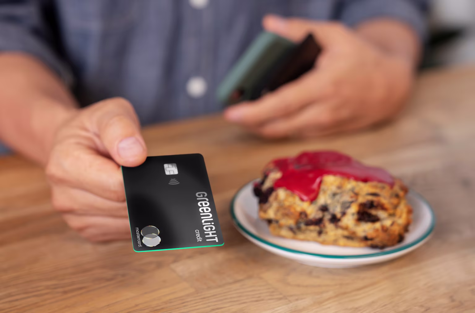 Man holding the Greenlight Family Cash Card in his hand to pay for the scone sitting on the table