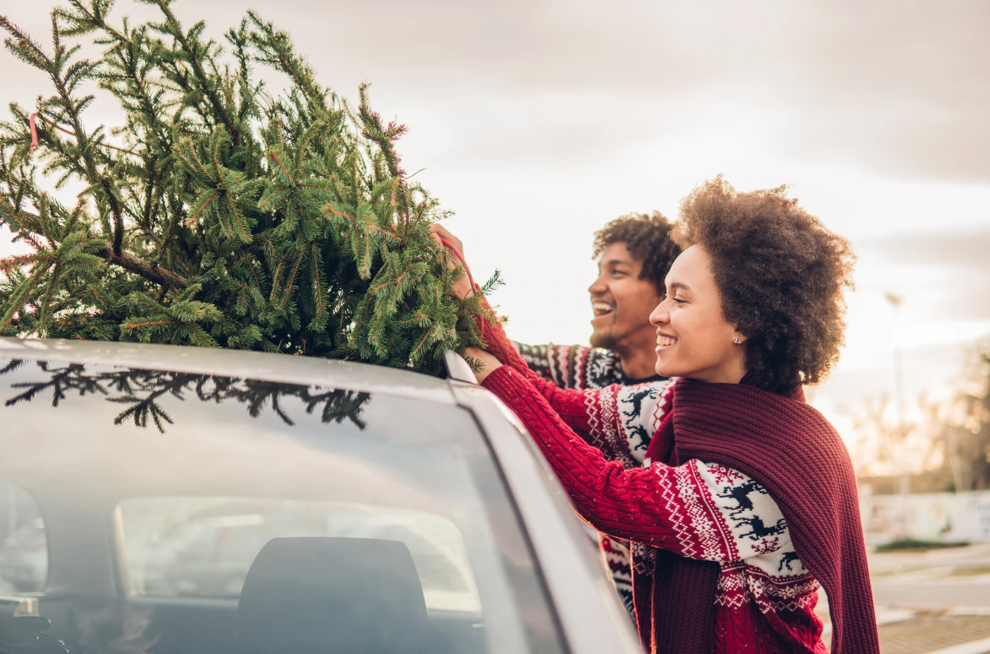 Mom and dad put Christmas tree on top of their car before traveling to see family for the holidays