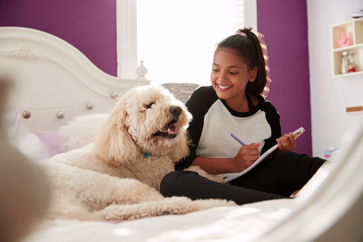 Girl writing in a notebook while looking at a dog