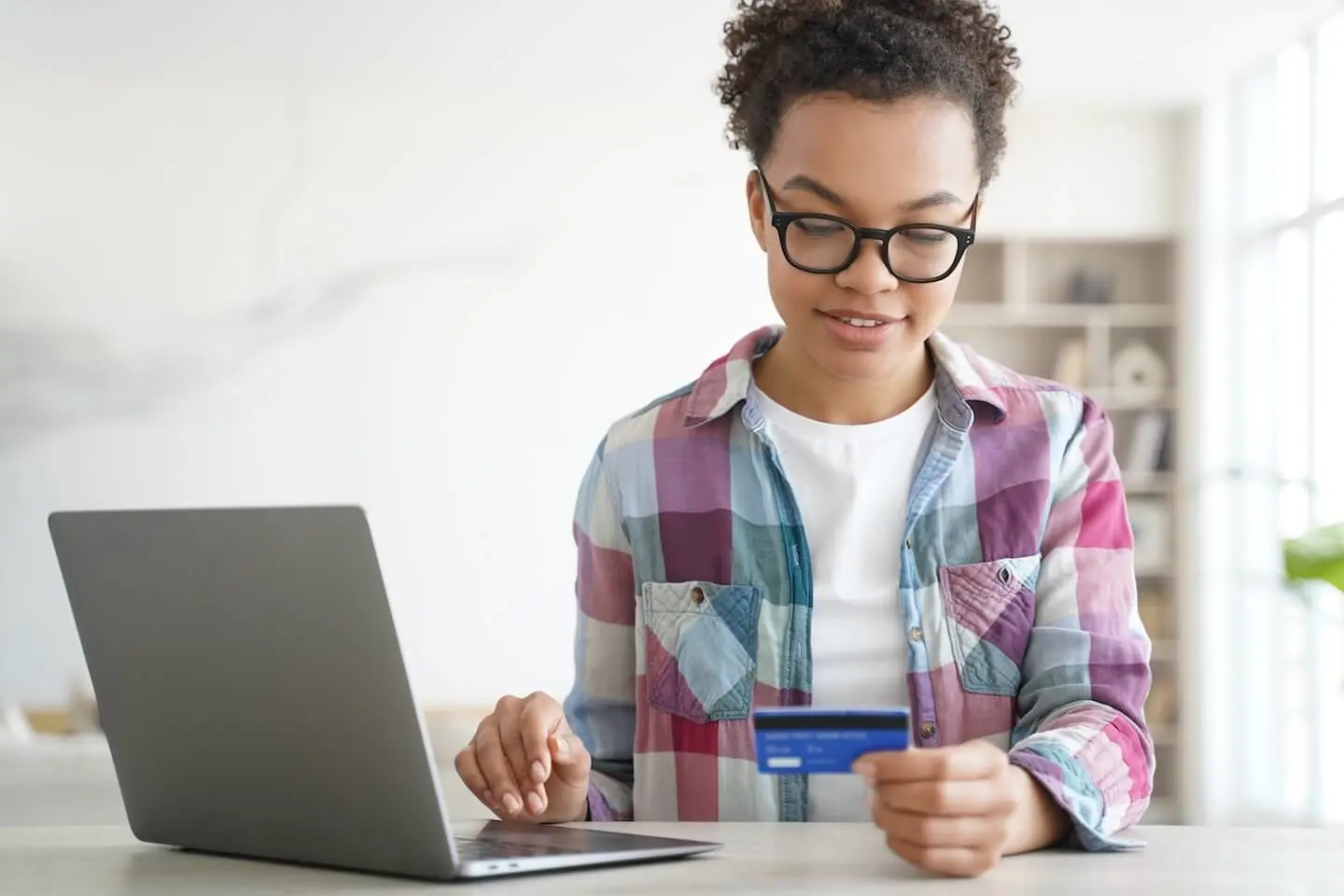 Young woman at her laptop holding a credit card for teens.