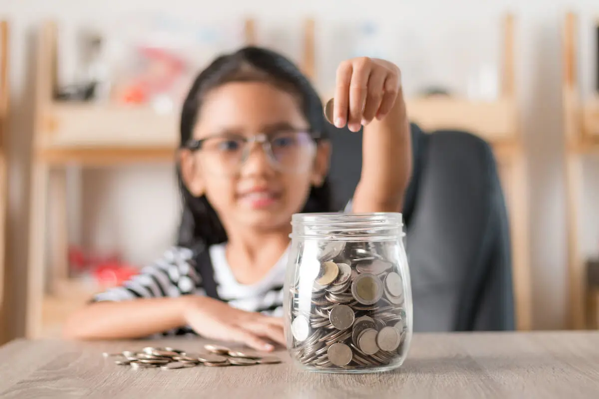 A young girl puts coins into a jar