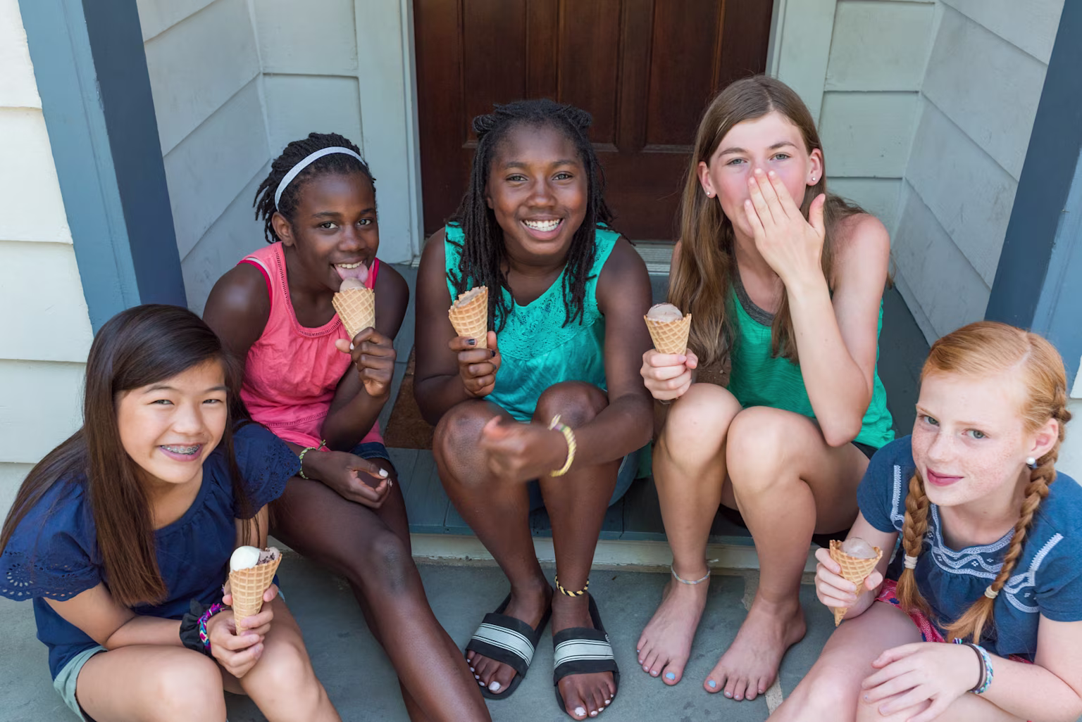 Group of girls sitting outside together eating ice cream cones.