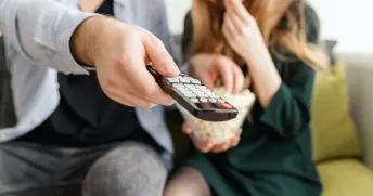 Par som sitter i en grön soffa hållandes i popcorn och fjärrkontroll.