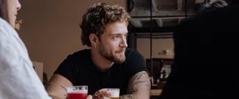 Fokus på en man med tatueringar som dricker öl på en bar med två vänner