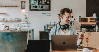 Ung man sitter och arbetar vid sin dator på ett café.