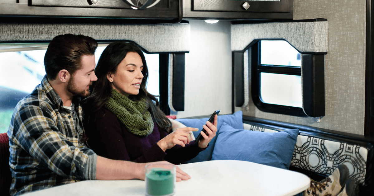 Man och kvinna sitter i en husvagn och tittar på kvinnans mobiltelefon. 
